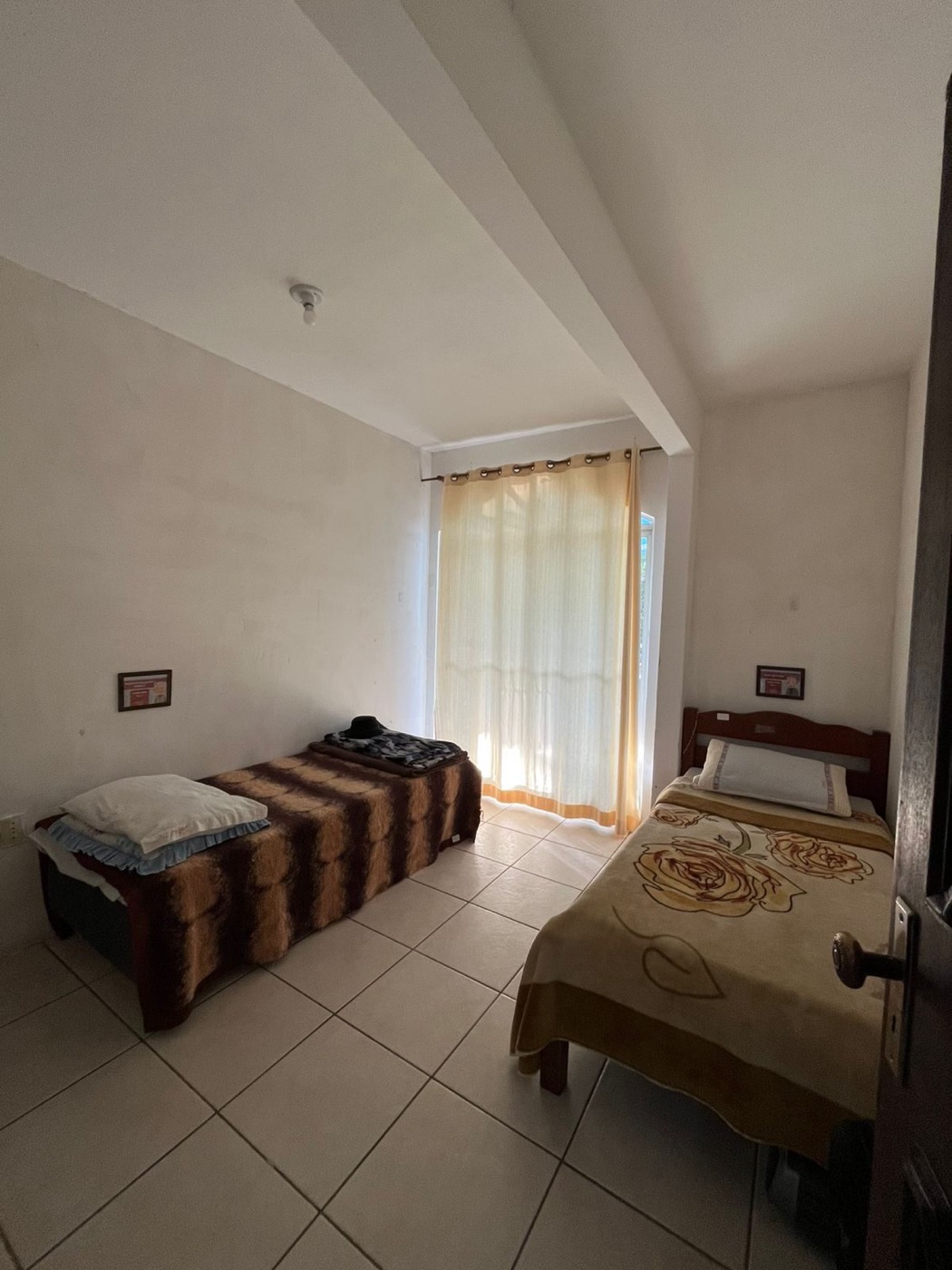Quarto duplo do Residencial Sagrada Família com duas camas arrumadas e luz natural, em São José, perto de Palhoça